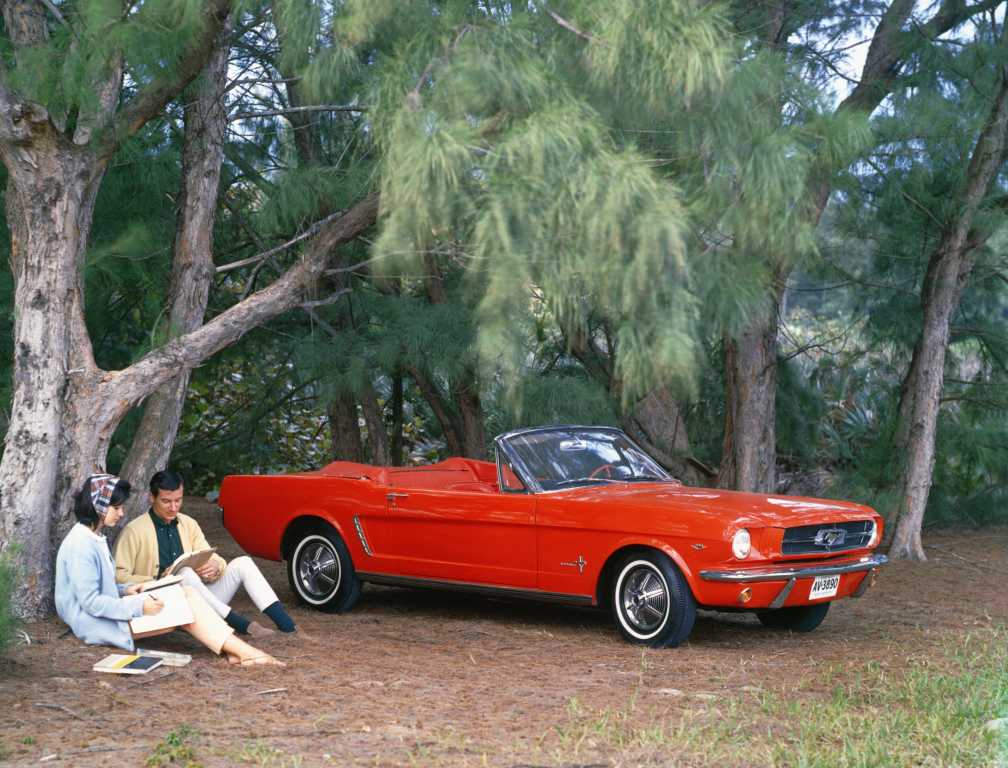 Ford Mustang convertible rouge à coté de deux personnes sous un arbre